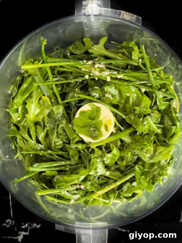 Zesty Mediterranean Pasta with Garden Herb Dressing 5 A mix of fresh herbs like parsley, basil, and arugula, along with garlic cloves, in the base of a large food processor, ready to be blended for the vinaigrette.