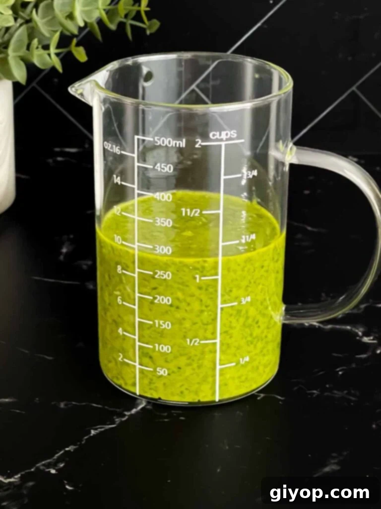 Zesty Mediterranean Pasta with Garden Herb Dressing 6 The finished fresh herb vinaigrette in a clear glass measuring cup, showing its vibrant green color and smooth, emulsified texture on a dark background.