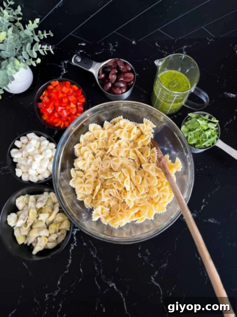 Zesty Mediterranean Pasta with Garden Herb Dressing 7 Cooked Farfalle pasta in a glass bowl, with prepped Mediterranean salad ingredients like olives, bell peppers, and mozzarella balls arranged around it, ready for mixing.