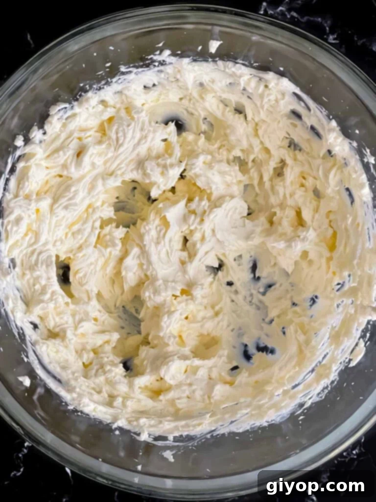 Mediterranean Olive Cheese Ball 4 Room temperature cream cheese, beaten until smooth and creamy, in a clear glass mixing bowl, ready for additional ingredients.