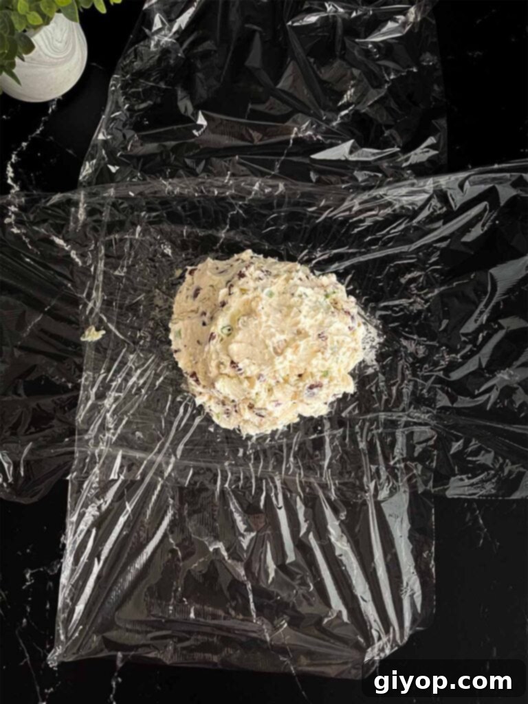Mediterranean Olive Cheese Ball 6 The olive cheese ball mixture placed neatly in the center of two pieces of plastic wrap on a dark surface, ready for shaping.