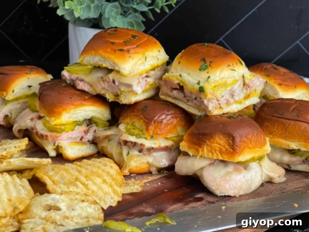 Roll-cut pork tenderloin Cuban sliders stacked on a wooden board with pickles.