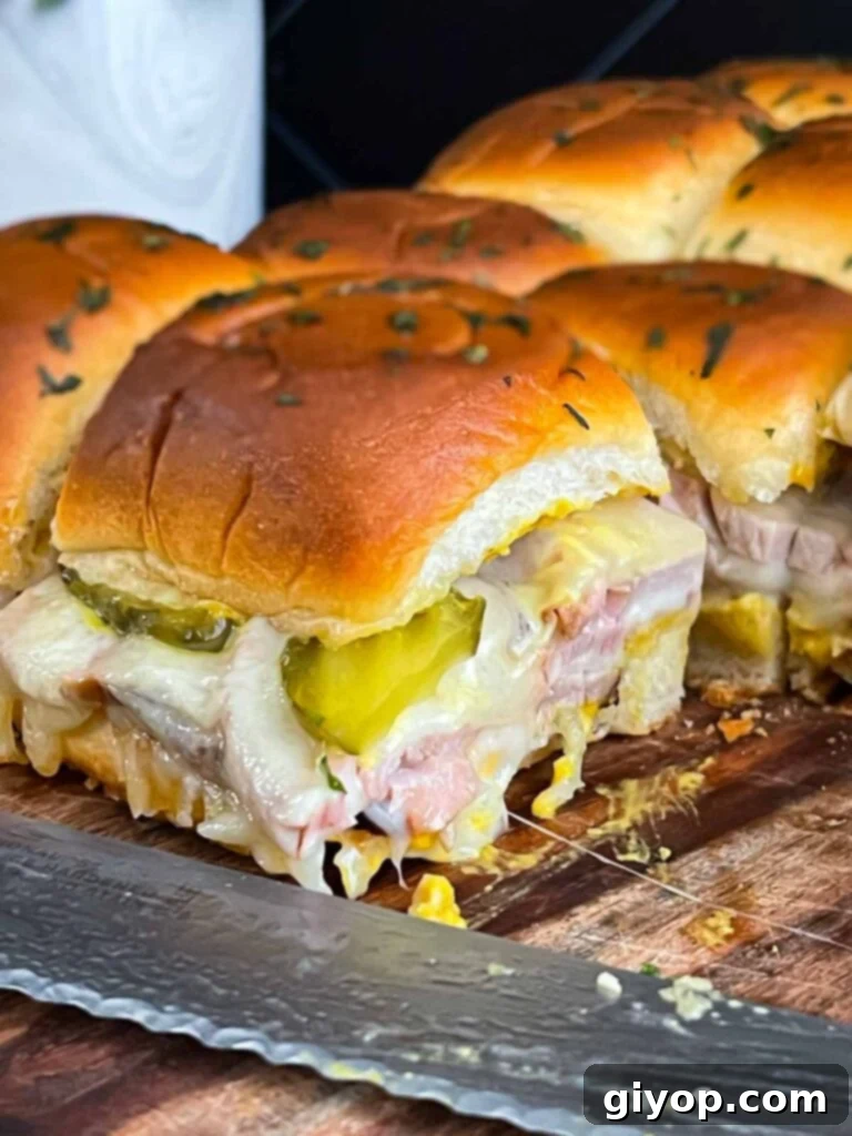 Close-up of a single roll-cut pork tenderloin Cuban slider, showing the layers of meat, cheese, and pickles.