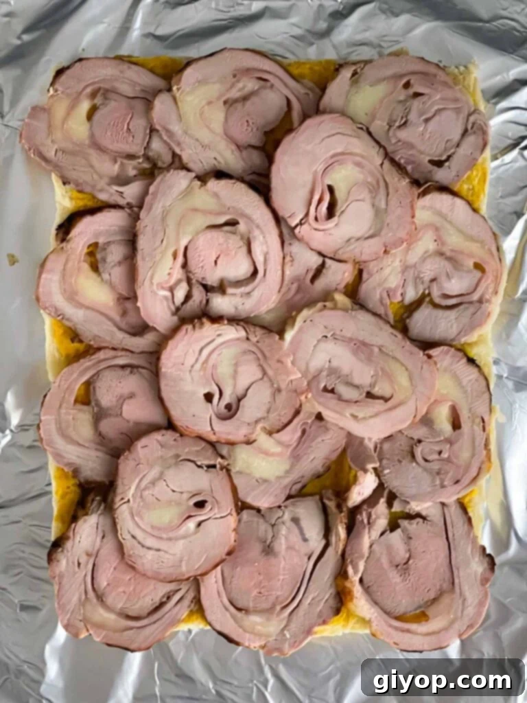 Thinly sliced grilled pork tenderloin roulade being stacked onto slider rolls.