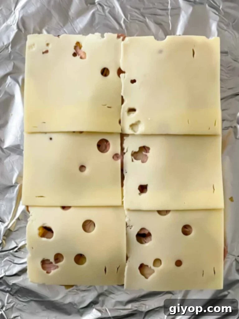Swiss cheese slices being placed on the pork tenderloin for the Cuban sliders.