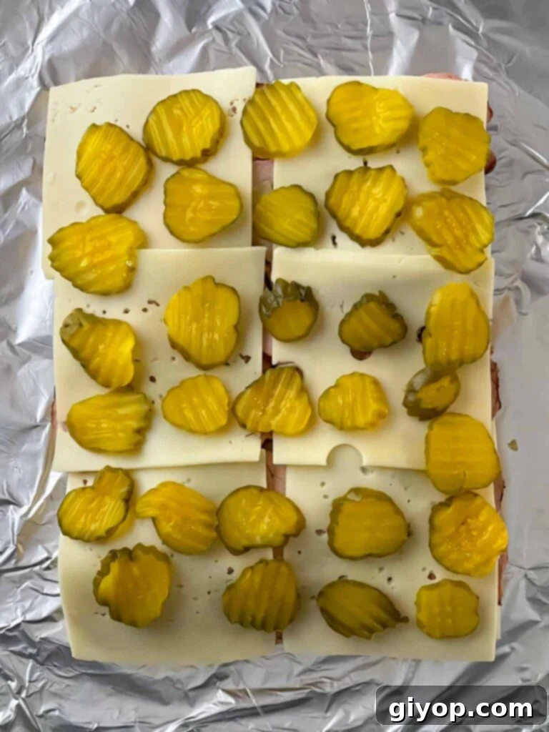 Dill pickles being added as the final layer on the pork tenderloin sliders.