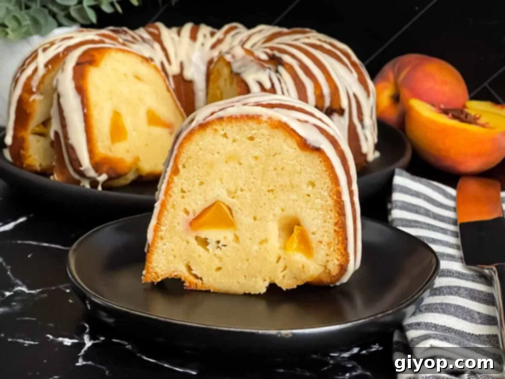 A perfectly sliced peach pound cake with a generous peach glaze, resting on a dark plate against a complementary dark background. The cake's texture looks moist and tender, showcasing the rich peach color.
