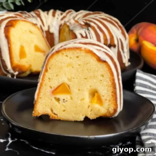 A close-up shot of a peach pound cake slice on a dark plate, showcasing its moist texture, visible peach chunks, and a rich, shiny glaze.