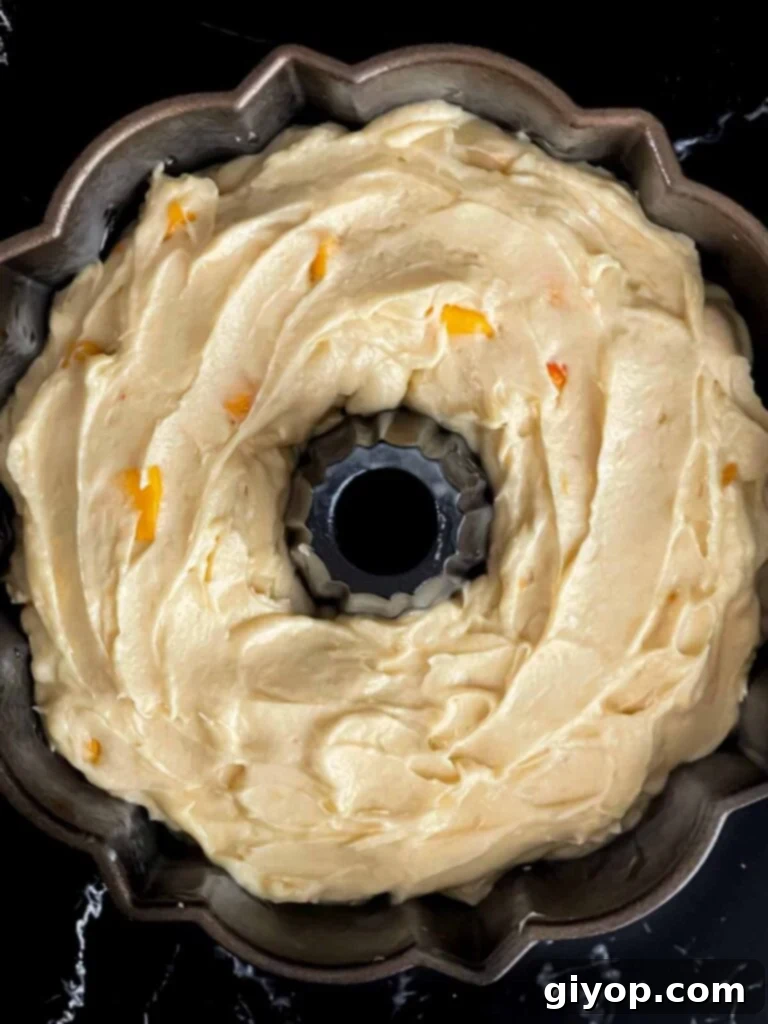 The smooth peach pound cake batter evenly spread in a bundt pan, ready for baking to golden perfection.