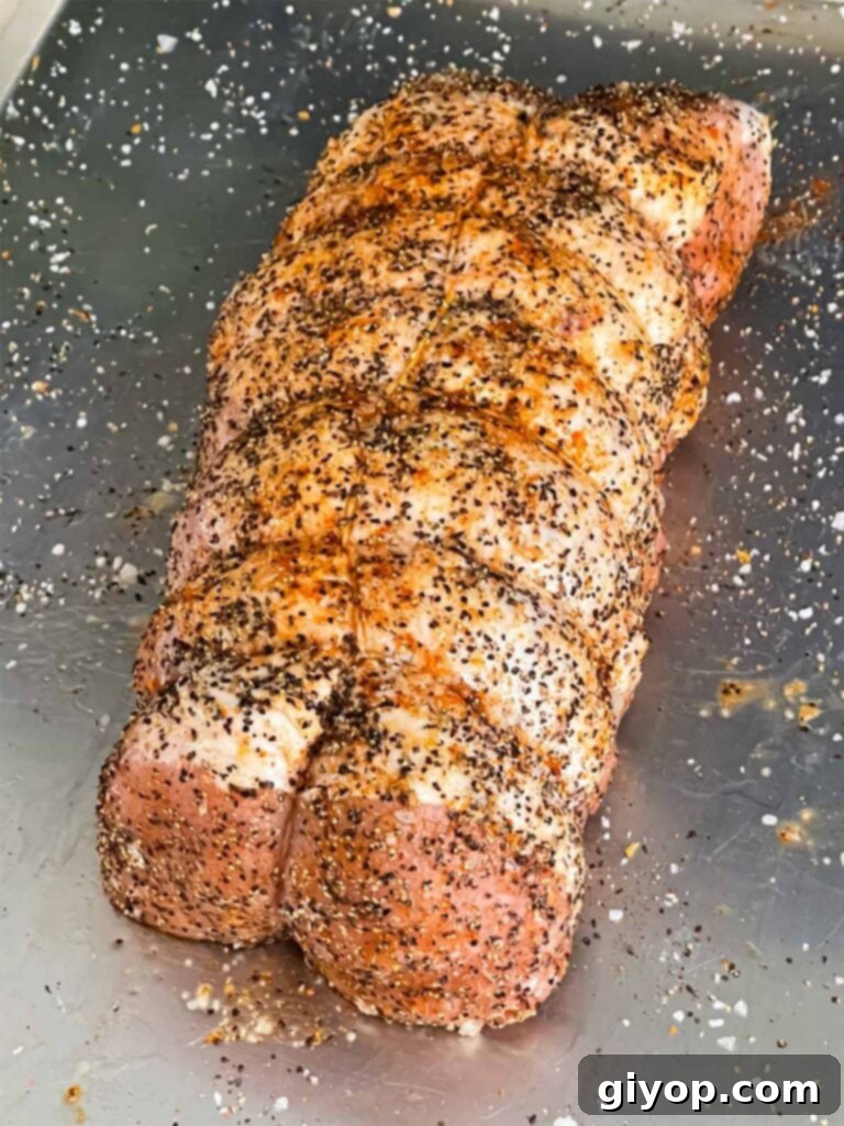 Texan Pit Smoked Pork Loin 4 A pork loin trussed and seasoned with salt and black pepper on a baking sheet.