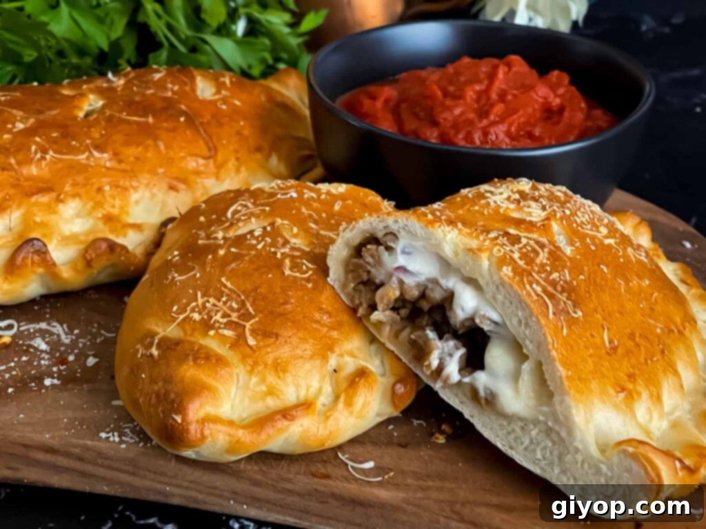 A freshly baked Italian sausage calzone on a wooden cutting board, ready to be sliced, with a side of dipping sauce.