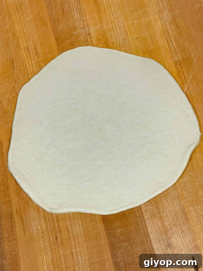 A rolled-out circular piece of calzone dough on a floured surface.