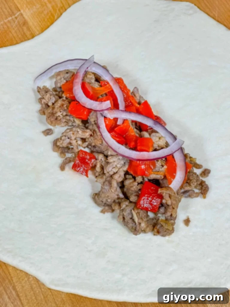 A calzone being assembled with sausage, peppers, and cheese on one half of the dough.