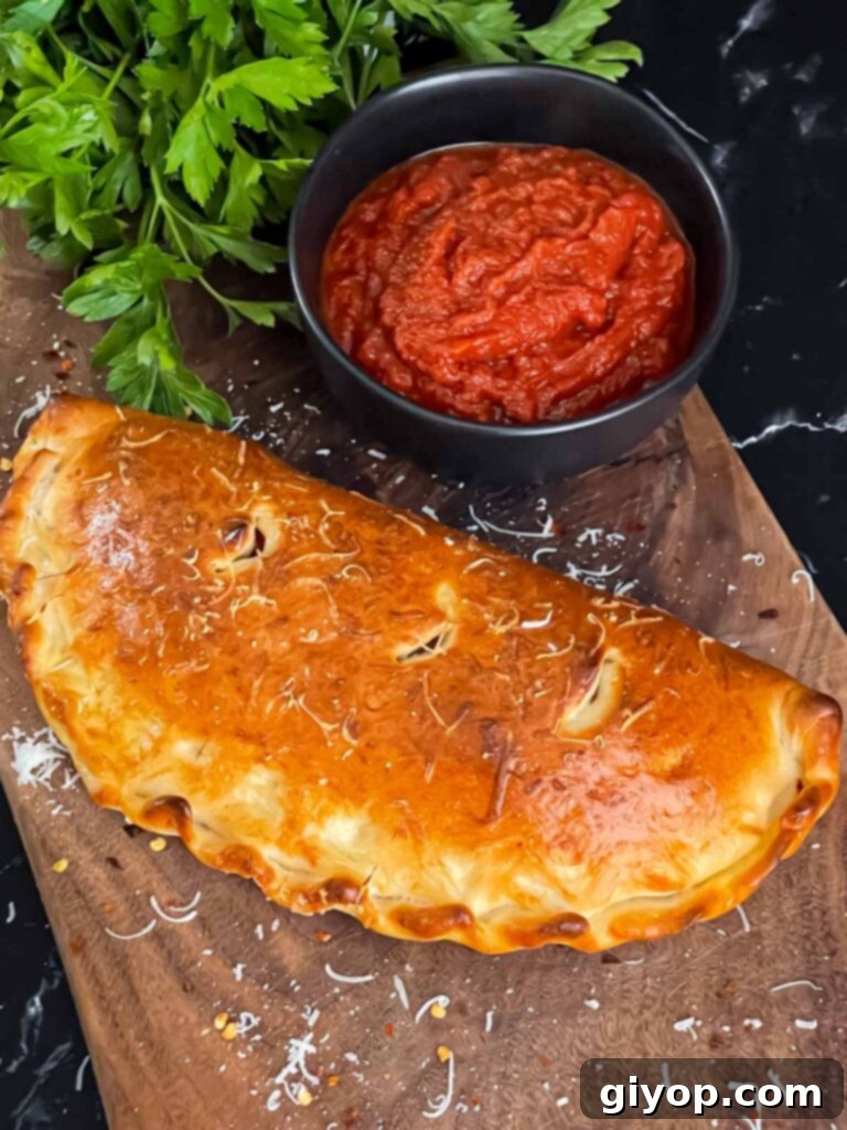 A sliced Italian sausage calzone on a cutting board with a bowl of dipping sauce.