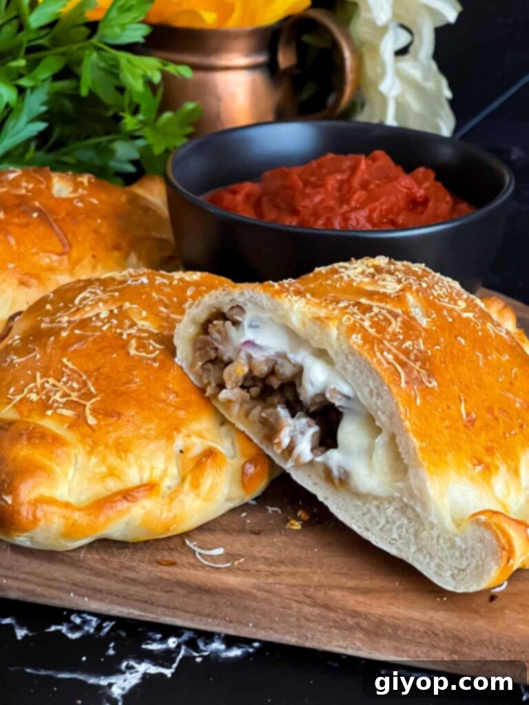A perfectly baked Italian sausage calzone, sliced open to reveal the cheesy filling, on a cutting board.