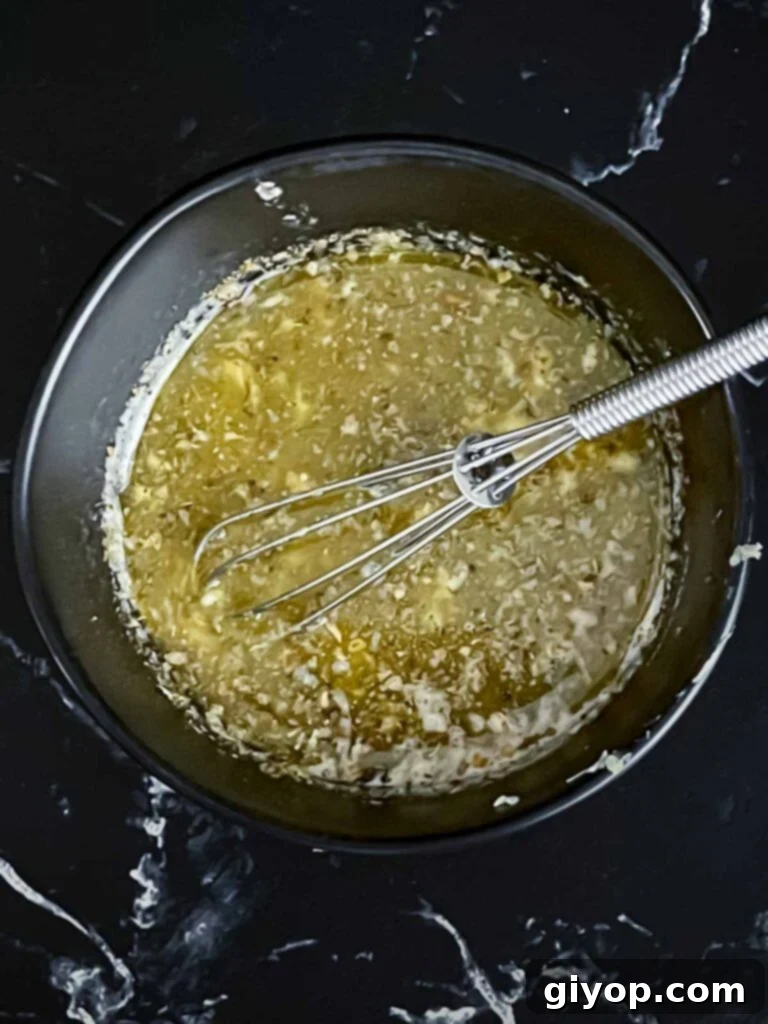 Slow cooker garlic parmesan potatoes herb butter mixture in a dark bowl on a dark surface.