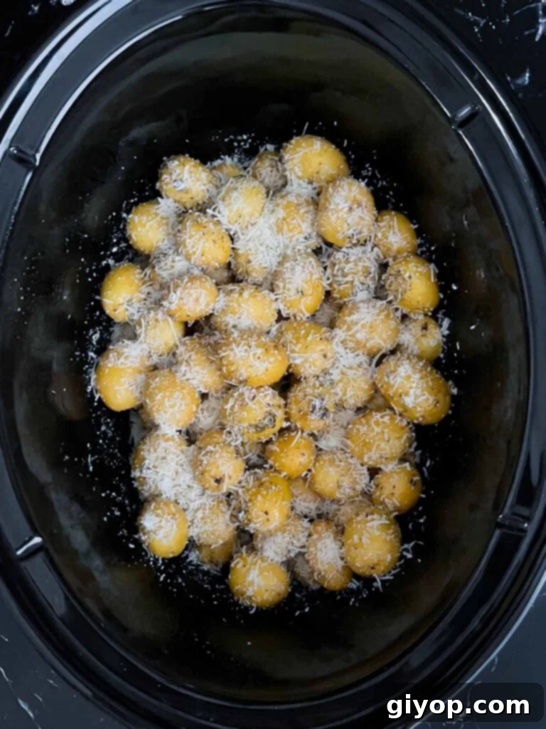 Shredded parmesan sprinkled over the seasoned potatoes in the crock of a slow cooker.