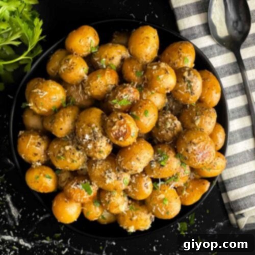 Slow cooker garlic parmesan potatoes in a dark bowl garnished with parsley and parmesan cheese.