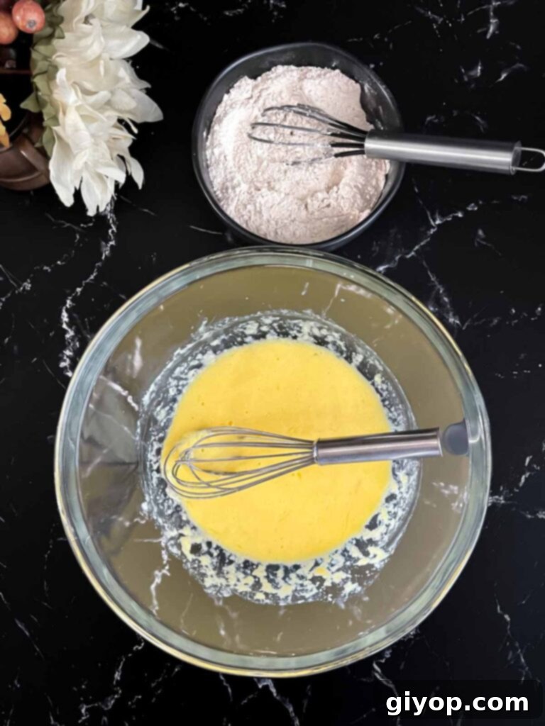 Cinnamon Apple Bliss 5 Wet ingredients whisked in a glass bowl and dry ingredients whisked in a dark bowl for the apple fritters recipe.