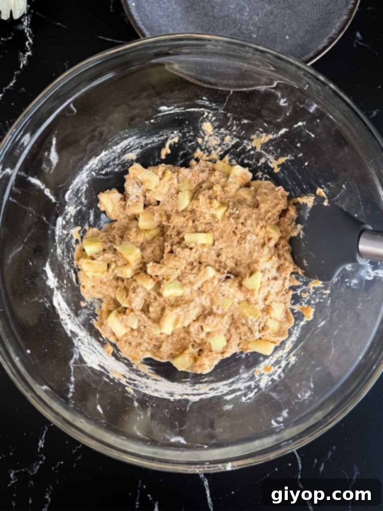 Cinnamon Apple Bliss 6 Apple fritters batter mixed in a glass mixing bowl on a dark surface.