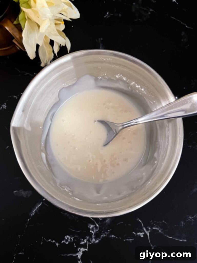 Cinnamon Apple Bliss 9 Apple fritters glaze mixed in a metal bowl on a dark surface.