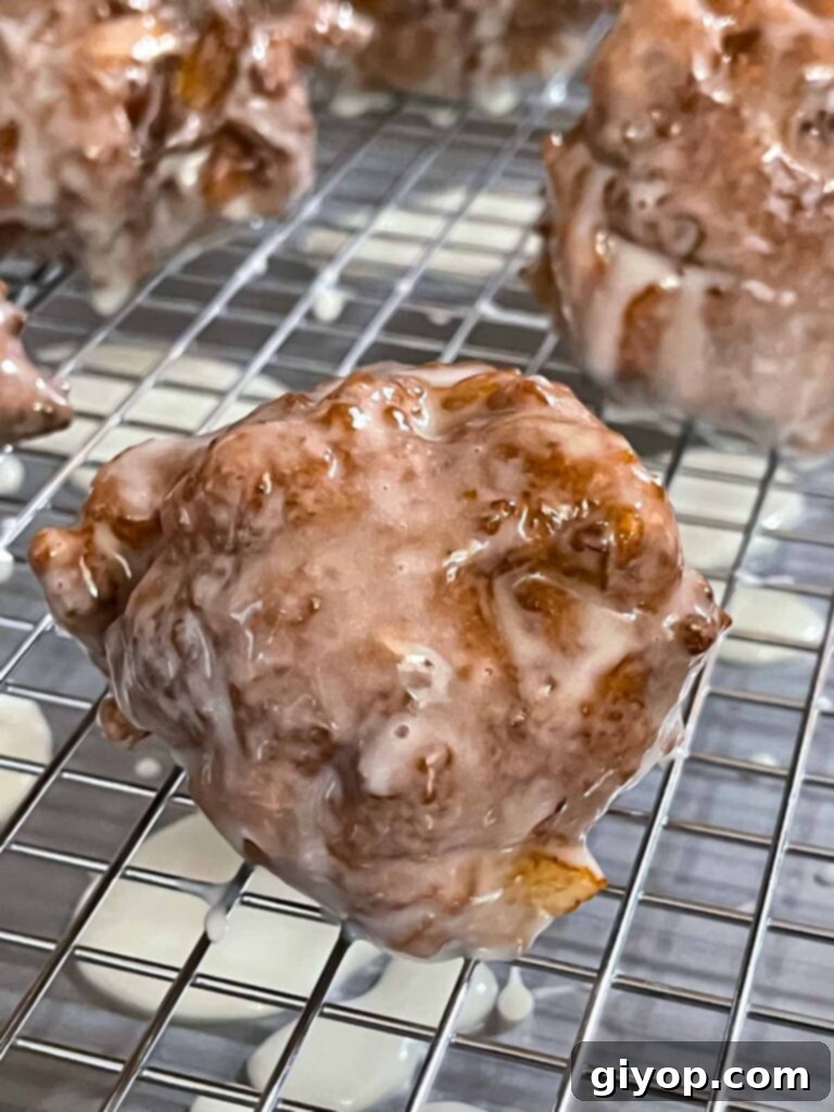 Cinnamon Apple Bliss 10 Glazed apple fritters on a wire rack over a baking sheet.
