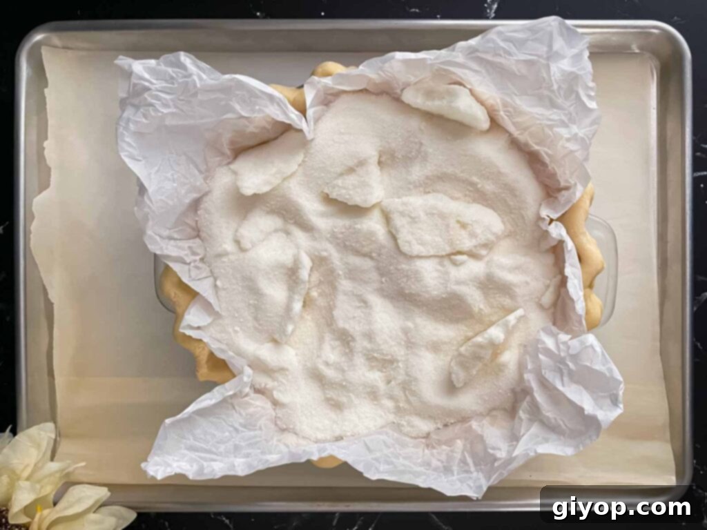 A golden-brown homemade pie shell, par-baked and filled with sugar acting as pie weights, resting on a baking sheet.