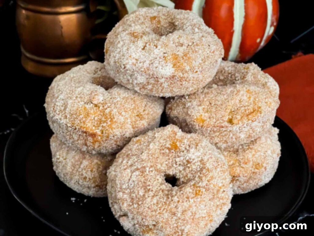 Baked pumpkin donuts stacked on a dark plate, ready to be enjoyed.