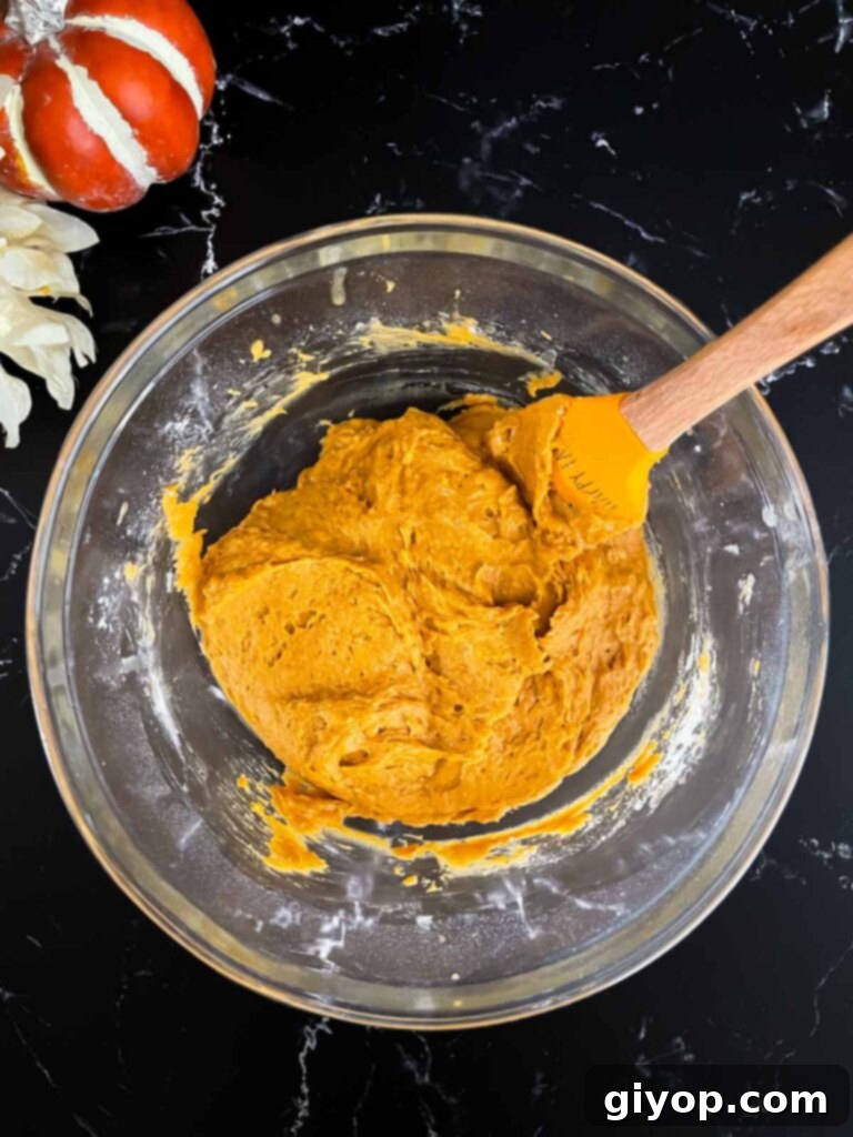 Baked pumpkin donuts batter mixed in a glass bowl on a dark surface.
