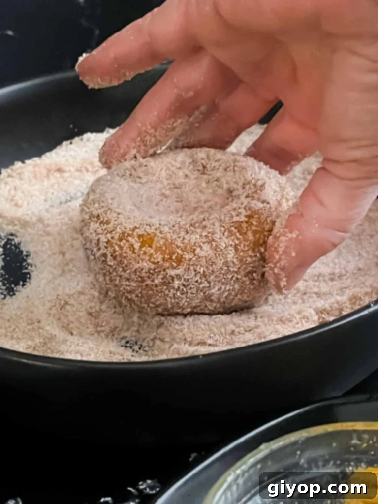 Baked pumpkin donut being rolled in the cinnamon sugar mixture.