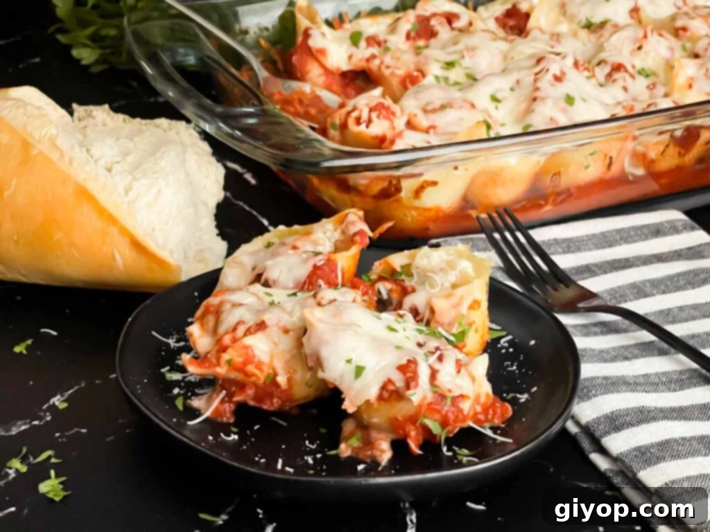 Italian stuffed shells on a black plate with some bread and a casserole dish in the background.