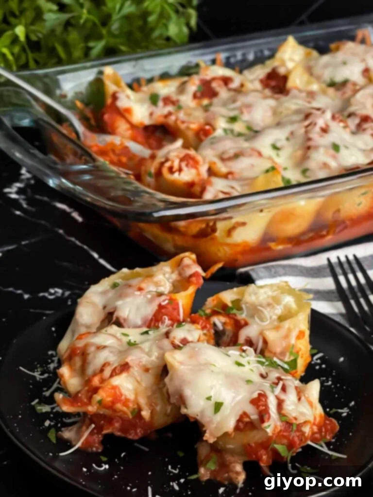 Italian sausage stuffed shells on a black plate with a casserole of it in the background.