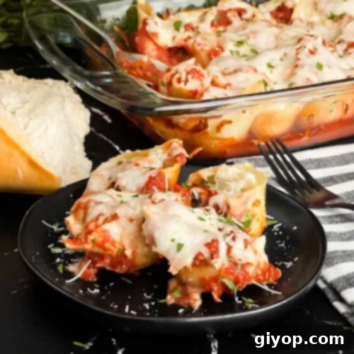 Italian stuffed shells on a black plate with some bread and a casserole dish in the background.