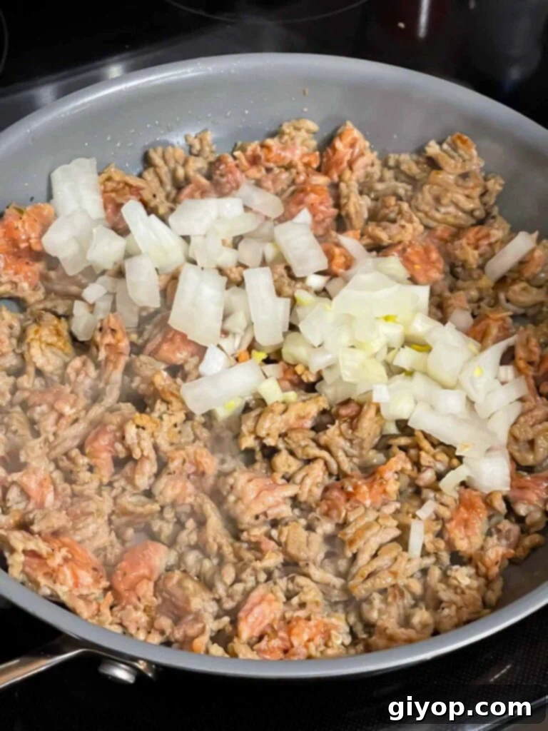 Onions added to Italian sausage in a skillet.