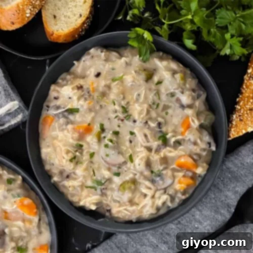 Soul-Warming Slow Cooker Chicken and Wild Rice Soup 12 Slow cooker chicken and wild rice soup in a dark bowl with a cut loaf of crusty bread.