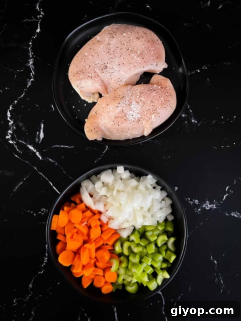 Soul-Warming Slow Cooker Chicken and Wild Rice Soup 4 Chicken breasts on a dark plate seasoned with salt and pepper, alongside a dark bowl full of diced onions, carrots, and celery, ready for the slow cooker.
