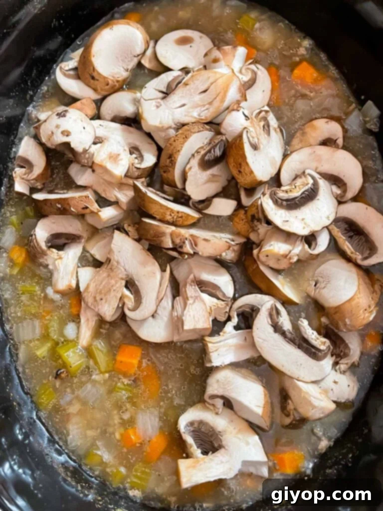Soul-Warming Slow Cooker Chicken and Wild Rice Soup 7 Sliced mushrooms being added to the slow cooker chicken and wild rice soup during the final cooking stage.