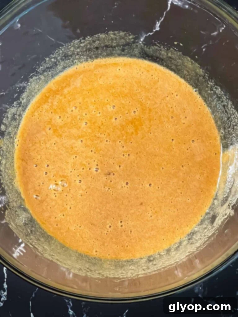 Eggs and sugars whisked in a glass bowl for zucchini bread recipe.