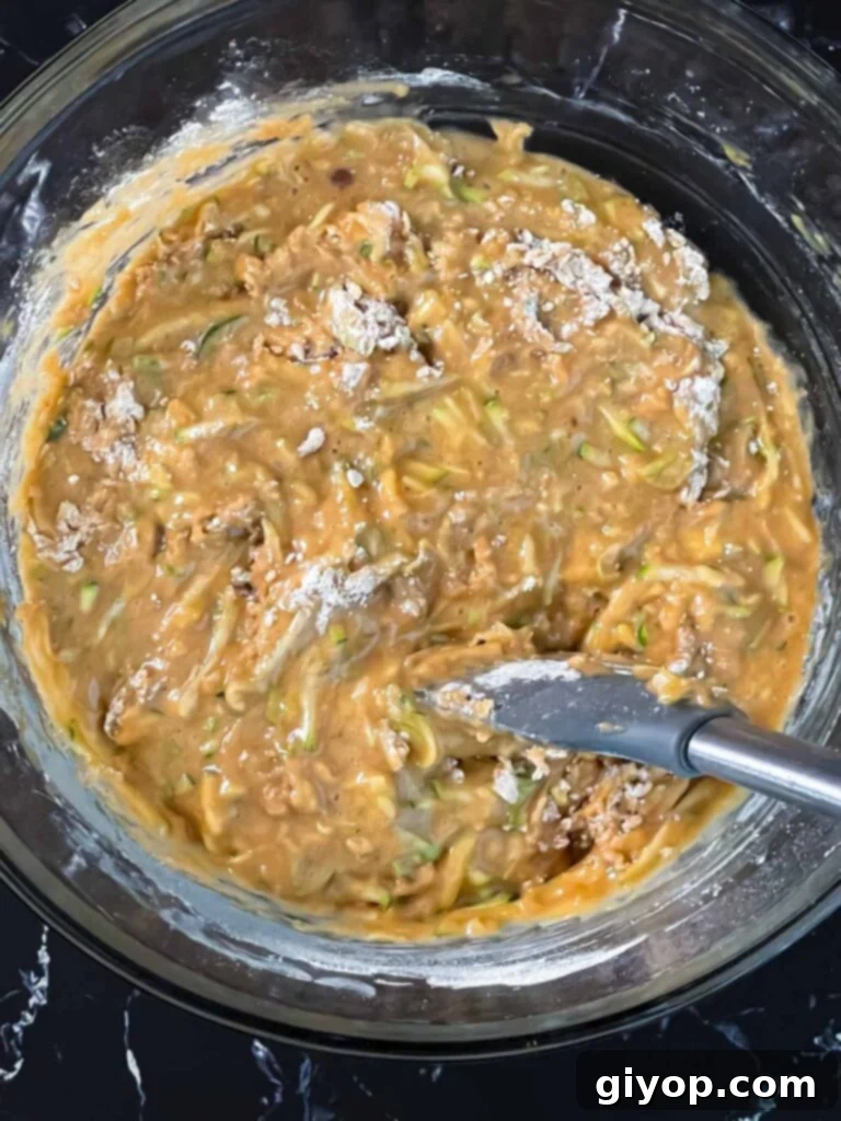Dry ingredients added to the wet ingredients in a glass bowl for zucchini bread.