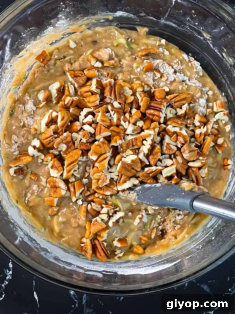 Chopped pecans added to the zucchini bread batter in a glass bowl.