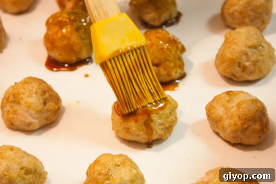 Baked firecracker chicken meatballs being brushed with sauce
