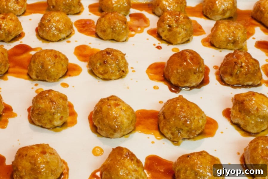 Firecracker chicken meatballs brushed with sauce on a parchment lined baking sheet.