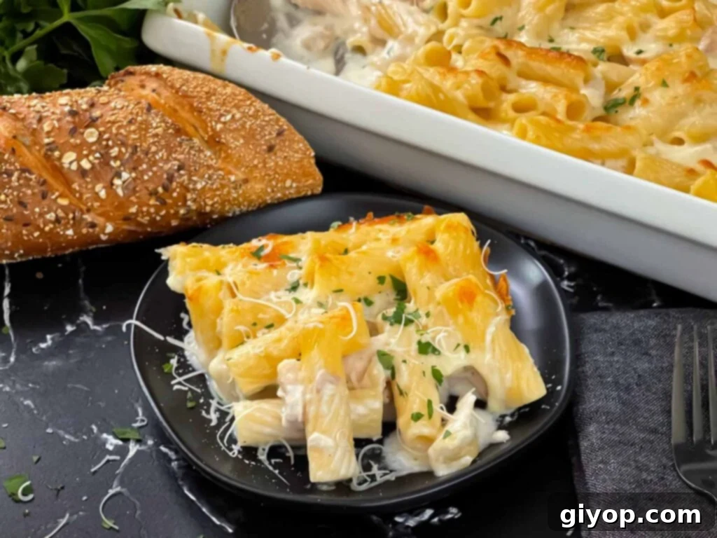 Chicken Alfredo Casserole in a white casserole dish with a serving on a black plate.