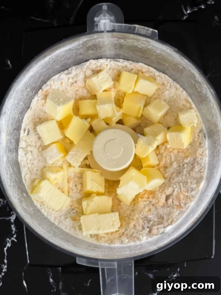 Savory Cheddar Herb Twists 6 Cold butter cubes being added to the flour and cheese mixture in a food processor, ready for pulsing.