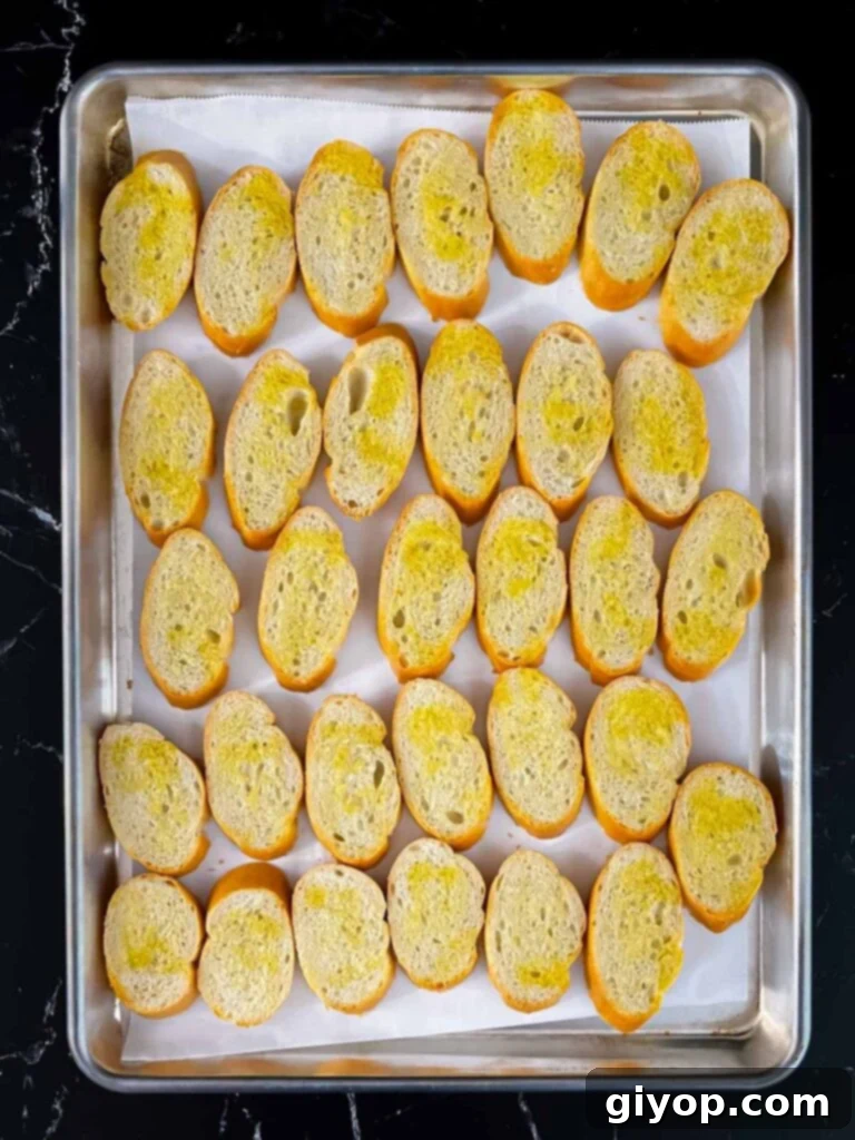 Baguette slices with olive oil arranged on a baking sheet, ready for toasting.