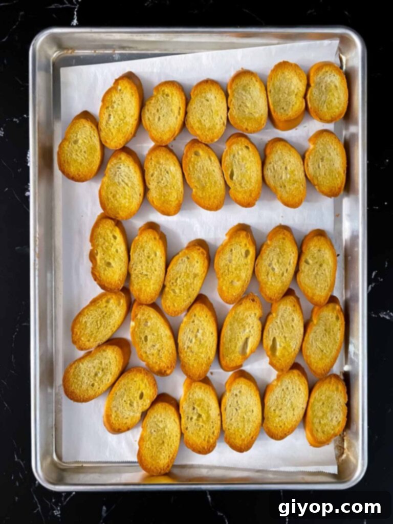 Perfectly toasted golden-brown baguette slices, brushed with olive oil, cooling on a baking sheet.