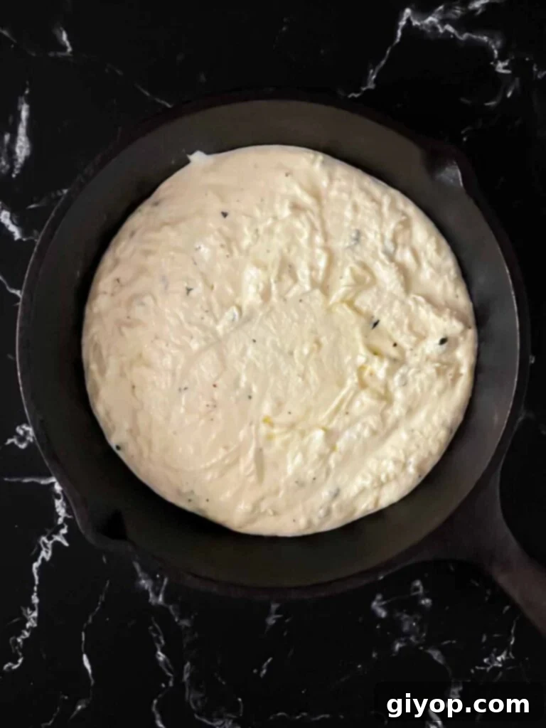 The mixed ricotta dip spread smoothly into a cast iron skillet, ready for its cheese topping.