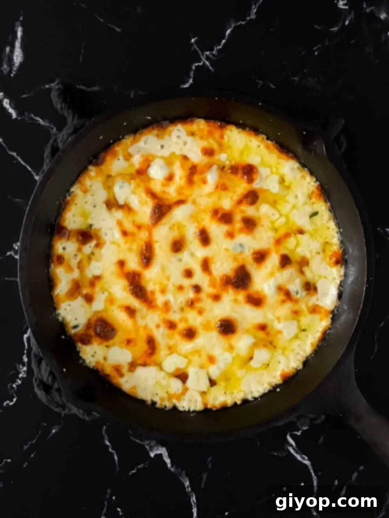 Freshly baked ricotta dip in a cast iron skillet, with a perfectly golden-brown and bubbly cheese crust, garnished with fresh thyme.