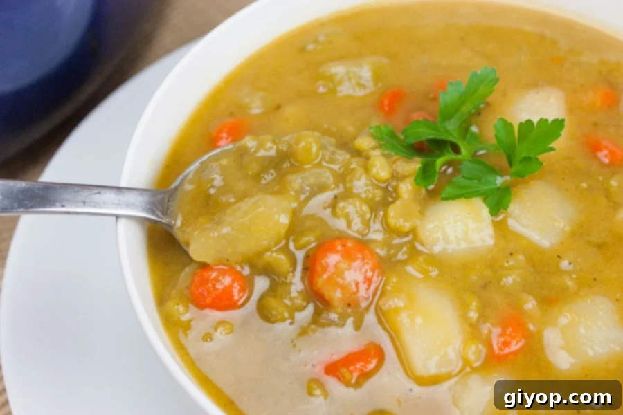 A steaming bowl of vibrant green vegan split pea soup, garnished with fresh herbs, served on a white table.