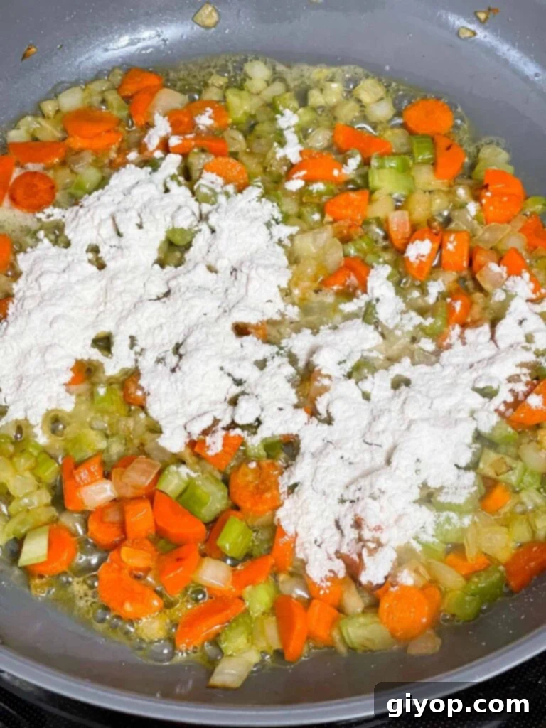 Flour being sprinkled into the cooked mirepoix in a skillet.